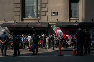 Migrants wait in line by the street, police watching