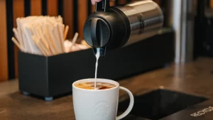 Person pouring milk into coffee at condiment bar