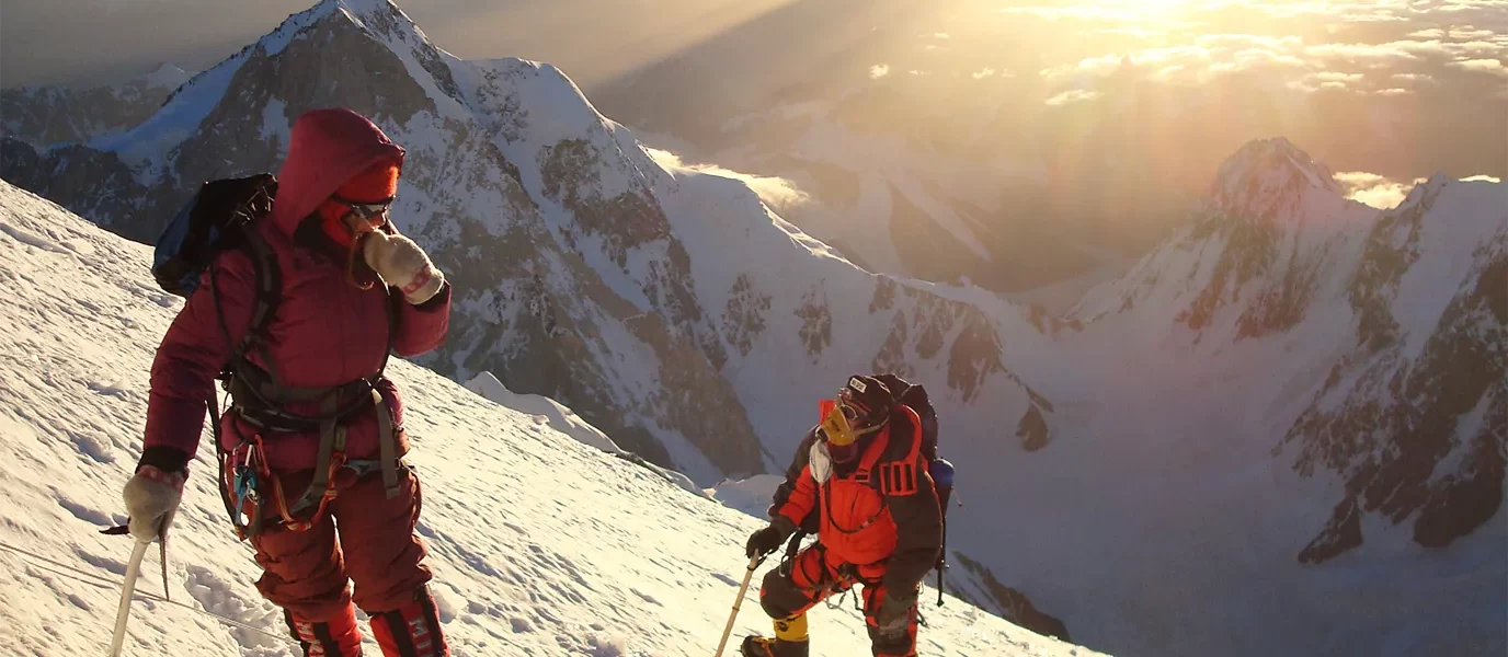 Two people climbing a snowy mountain in full gear on high, rugged peaks