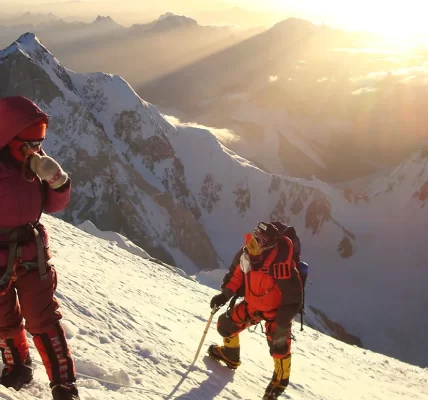 Two people climbing a snowy mountain in full gear on high, rugged peaks