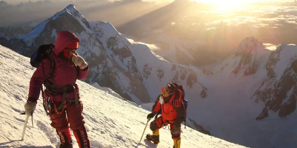 Two people climbing a snowy mountain in full gear on high, rugged peaks