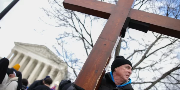 This photo depicts a man holding a cross outside of the U.S. Supreme Court building.